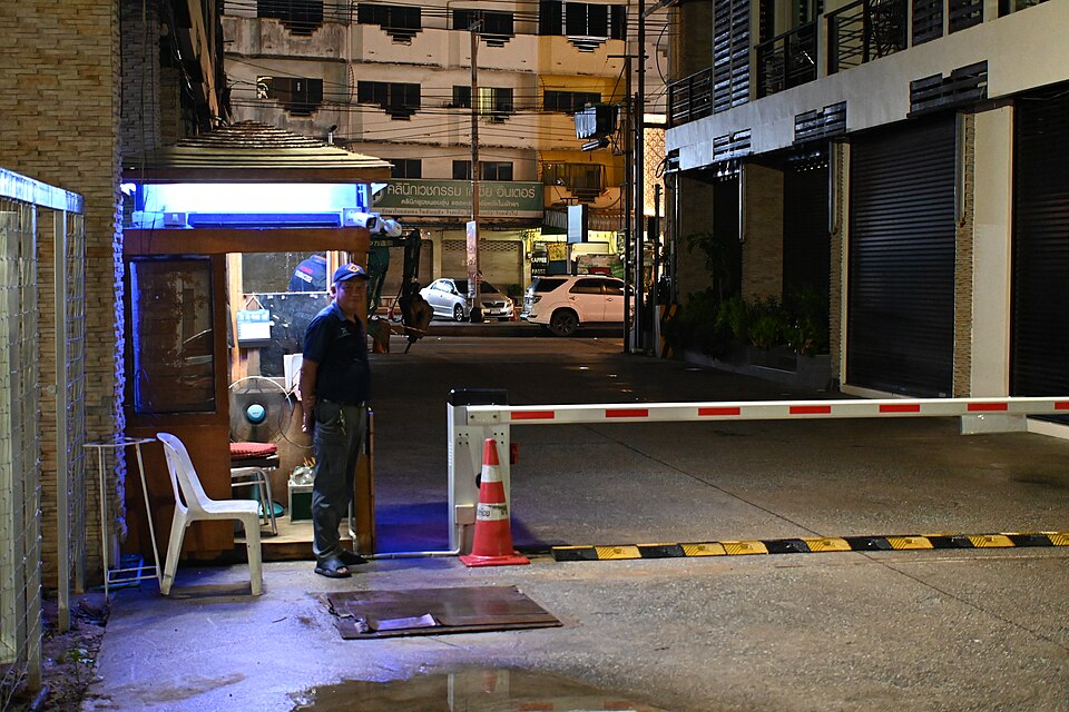 Security guard on duty beside the gated entrance to a residential complex at night